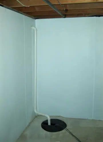 a basement with a sump pump in the corner and a white wall .