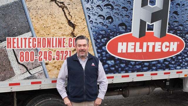 a man is standing in front of a truck with a helitech logo on it .