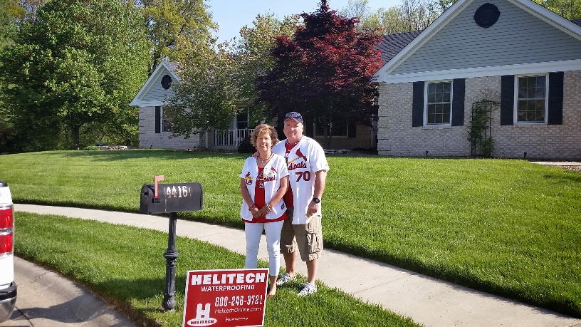 a man and woman are standing in front of a house with a Helitech sign in front of them