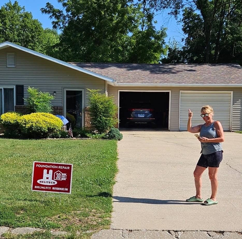 a woman is standing in front of a house with a sign that says `foundation repair for Helitech